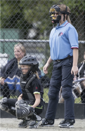 An umpire dressed in blue standing beside a back catcher at a softball game