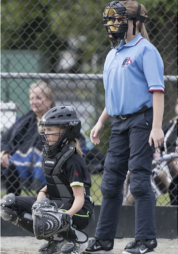 An umpire dressed in blue standing beside a back catcher at a softball game